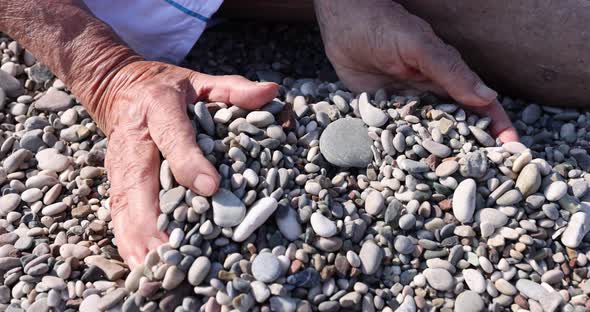 An Elderly Man Collects Pebbles in His Palms Seashore