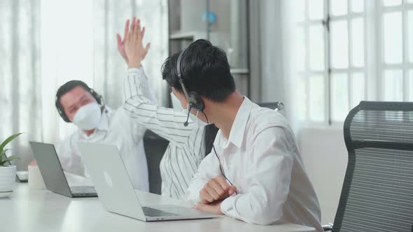 Three Asian Call Centre Agents Wearing Headsets, Masks, And Being Happy Due To Success Working