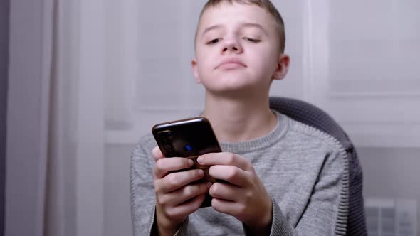 Child Sits in a Chair Holds a Smartphone in Hands Plays in Bedroom