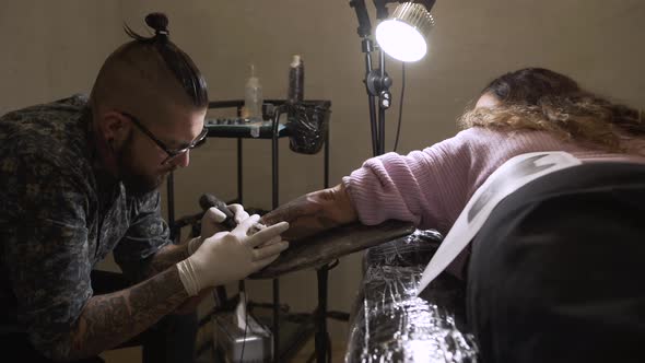 Young master making tattoo on skin of client