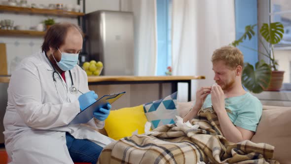 Young Doctor in Mask Writing Prescription During Home Visiting To Sick Man