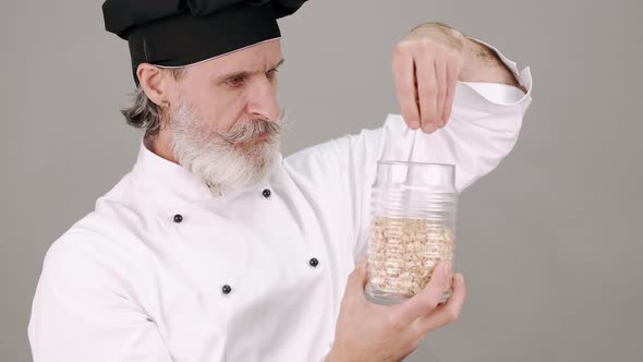Middle Aged Chef Man Pouring Cereals on Grey Background