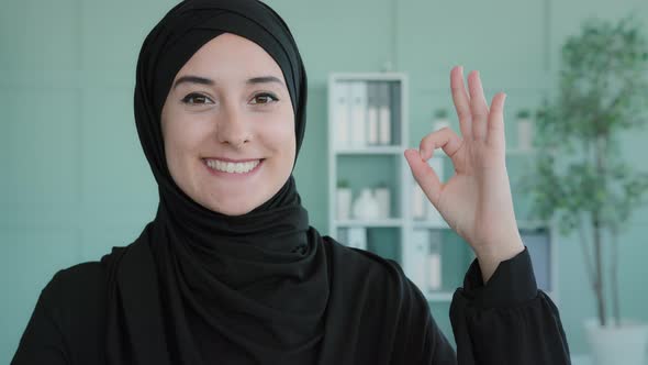 Portrait Indoors Muslim Islamic Girl Smiles Toothy Wide at Camera Showing Hand Ok Sign