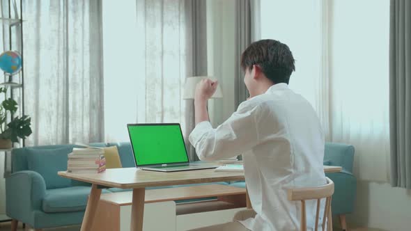 Hind View Of Asian Man Student Celebrating While Looking At Green Screen Computer At Home
