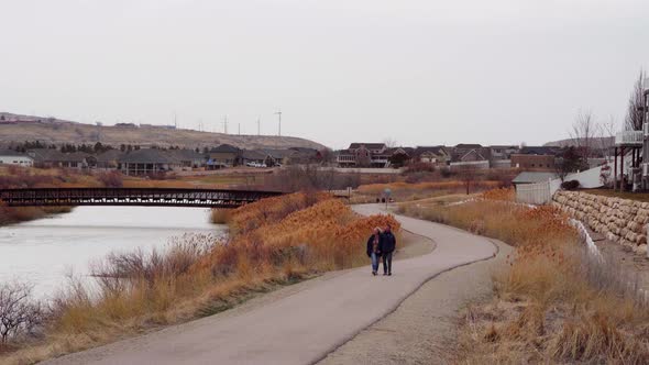 A young couple walking along a river side trail on a blustery overcast windy day in autumn - static