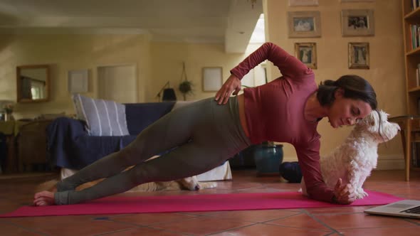 Caucasian woman exercising with her pet dog using laptop at home