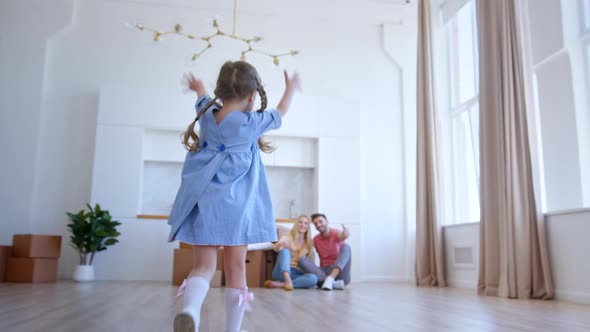 Happy preschooler girl in blue dress runs to parents and hugs among brown cardboard packages