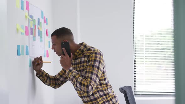 Mixed race man writing notes while on phone