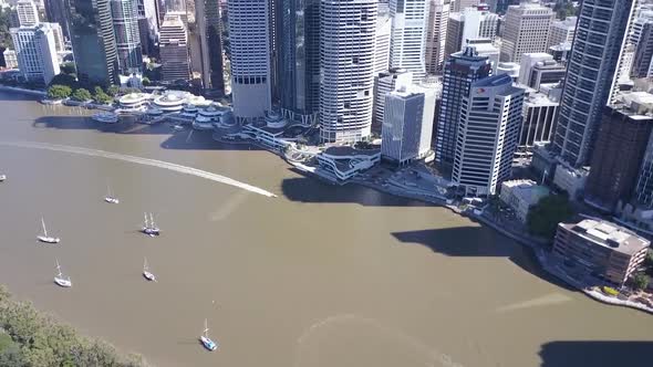 Aerial tilt shot of tall city buildings, jet-ski and sail boats along river Brisbane,  Queensland