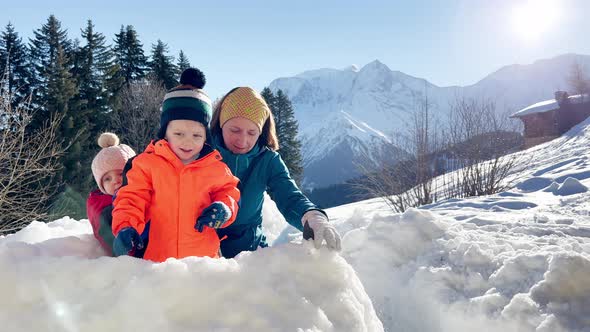 Baby Boy and Girl Play Snowball Sitting in the Snow Fortress