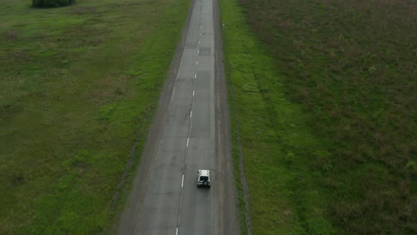 Aerial View of a Car Driving Along the Road Among Fields of Green Grass