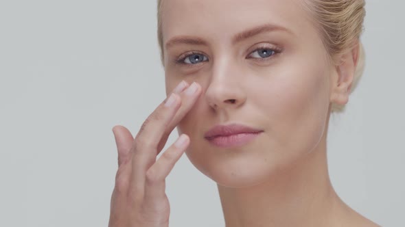 Studio portrait of young, beautiful and natural blond woman applying skin care cream. F