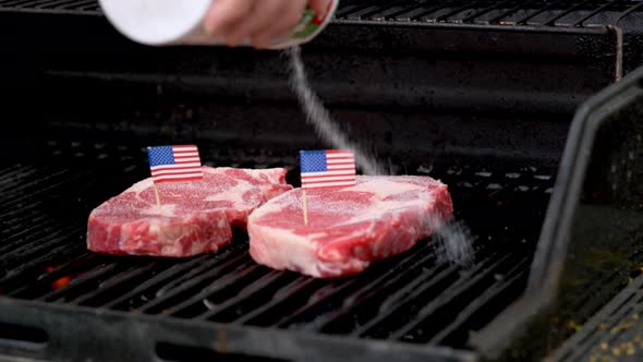 Two juicy rib-eye steaks sitting on the grill and cooking with two tiny American flags tooth picked