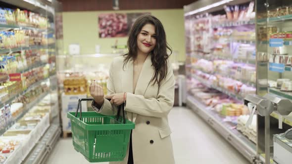 Confident Happy Woman with a Basket in Hand Smiling at the Camera in Supermarket