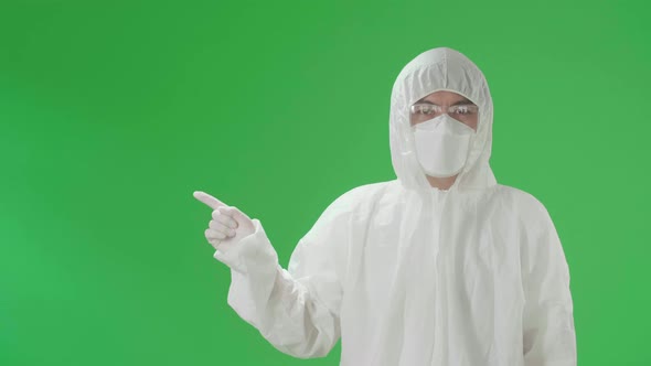 Asian Man Wear Protective Uniform PPE And Pointing To The Side In The Green Screen Studio