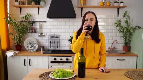 Relaxed Young Woman Poses with Glass of Red Wine Standing at Kitchen Table