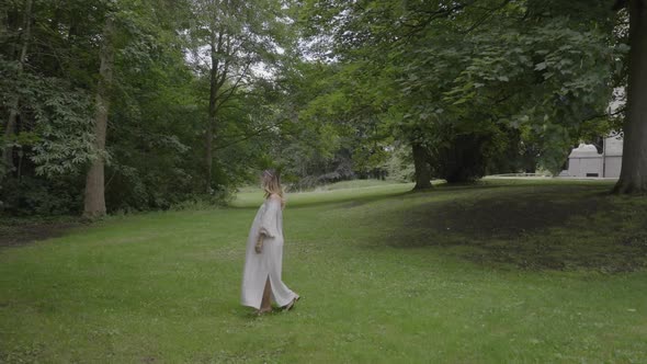 Pregnant young woman wearing a beautiful white dress walking through her lush green garden, concept