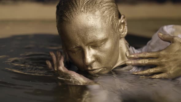 Woman with Face and Hair Covered Golden Paint in Bath or Pool Closeup View