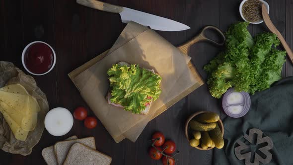 Flat Lay Video of the Chef's Hand Finalizes Sandwich with Salad and Cheese on the Wooden Board in