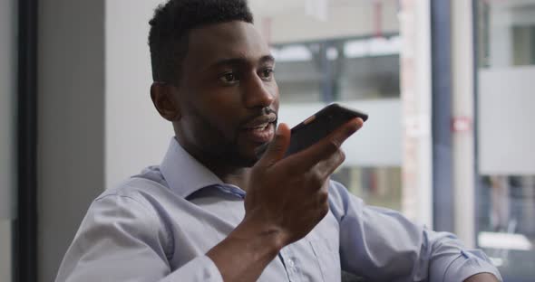 Worried african american businessman sitting in armchair talking on smartphone in modern office