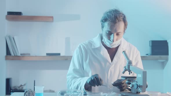 A Male Researcher Looks at the Mold Through the Eyepiece of a Microscope and Writes Down the Result