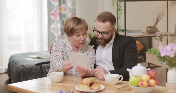 Good Looking Mature Mother and Adult Son Sitting and Watching Old Photos While Drinking Tea. Old