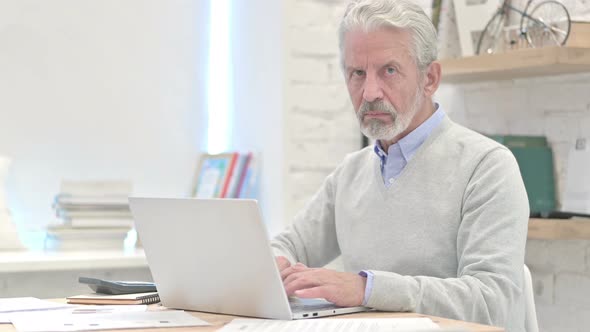 Thumbs Down By Old Man Sitting at Workplace