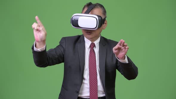 Mature Japanese Businessman Using Virtual Reality Headset Against Green Background