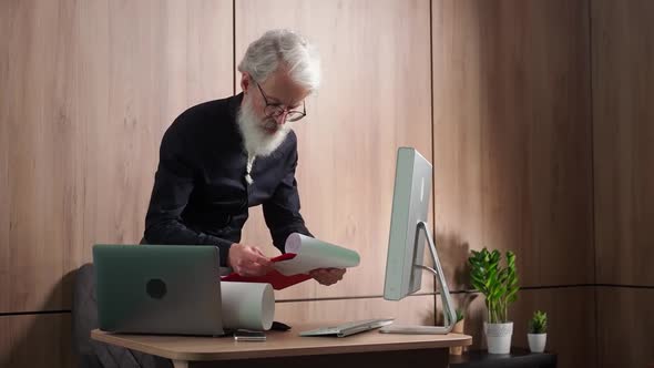 Grayhaired Caucasian Architect Checks Drawings of Objects and Uses a Desktop Computer for Design a