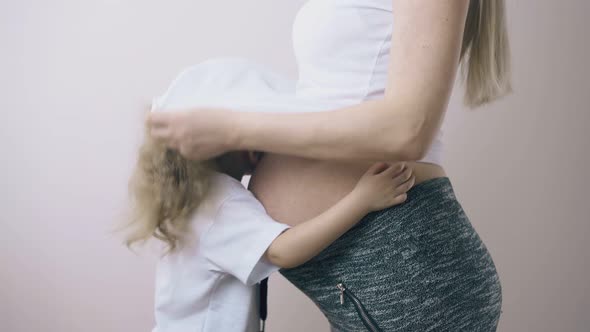 Girl Hides Head Under Pregnant Mommy Tshirt at White Wall
