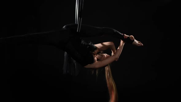 Slim Young Woman in Black Costume Hanging on Air Hoop Spinning Bending at Background