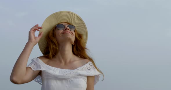 Portrait of a Woman in a White Tunic, Sunglasses and a Hat, She Walks Against the Sky and Smiles.