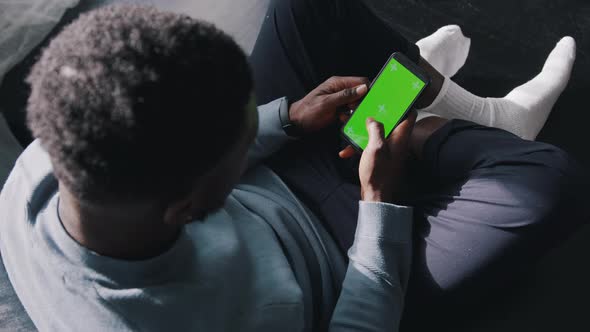 Man Sitting CrossLegged On The Couch Using A Cell Phone with a Green Screen