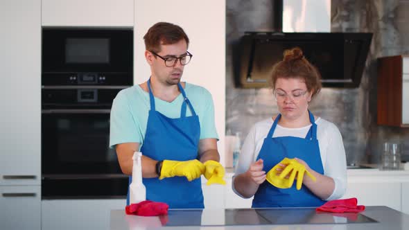 Two Young Professional Cleaners in Uniform Putting on Gloves Before Cleaning Modern Kitchen