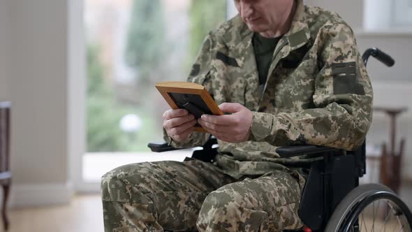 Unrecognizable Middle Aged Veteran in Military Uniform on Wheelchair Looking at Photograph and