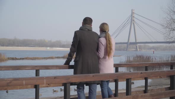 Back View of Adult Caucasian Couple Standing on Bridge in City Park and Talking. Elegant Man and