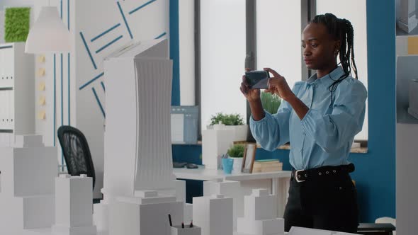 Woman Engineer Using Smartphone to Plan Layout of Building Model and Maquette