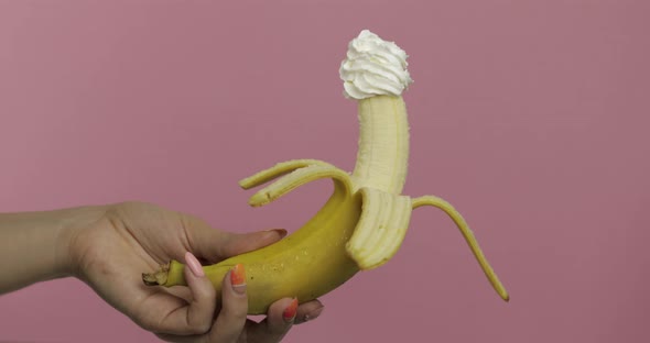 Woman Hand Holds Banana with Whipped Cream on Top of the Fruit