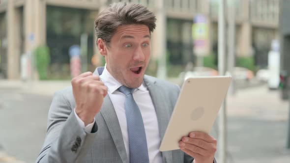 Middle Aged Businessman Celebrating on Tablet Outdoor