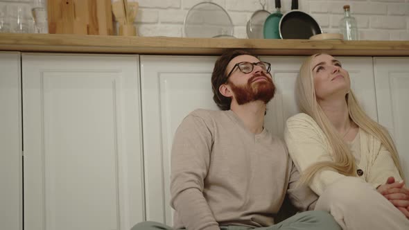 Portrait of Millennial Caucasian Couple Sitting on the Kitchen's Floor Bonding Cuddling and