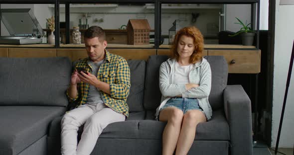 Man Is Sitting on Sofa, Using Smartphone, Woman Is Irritated By Man