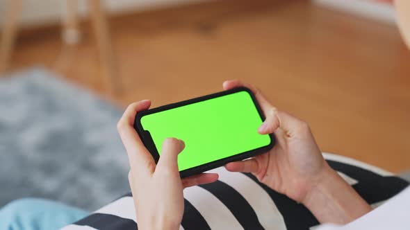 Woman holding in hands a smartphone with green screen for playing games