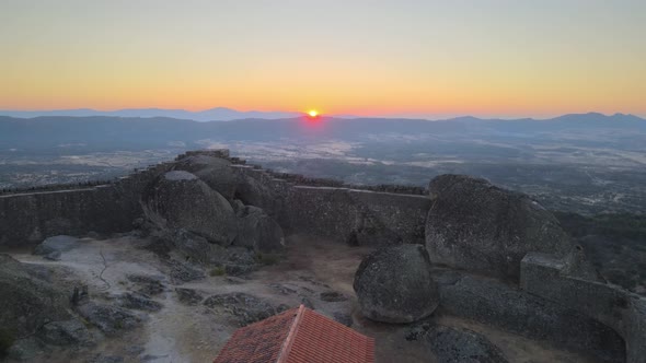 Cinematic aerial forward over Monsanto ruins while sun rises on horizon, Portugal