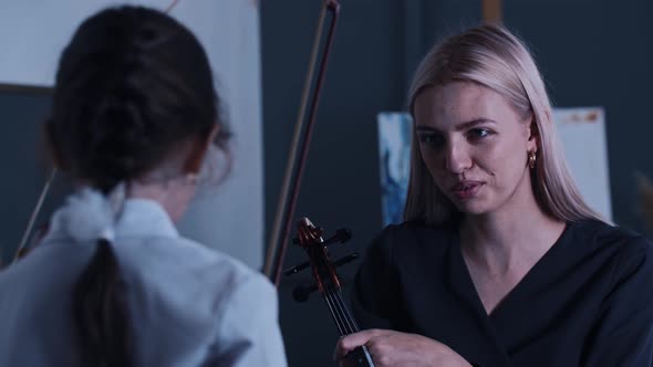 Young Blonde Woman Teacher Violin Player Talking to Her Little Girl Student
