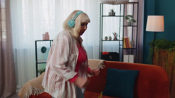 Happy Senior Woman in Wireless Headphones Dancing Singing on Cozy Couch in Living Room at Home