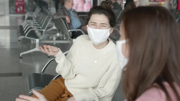 Two Women Tourists in Medical Mask Sitting in Airport Terminal at Safe Distance and Talking Before