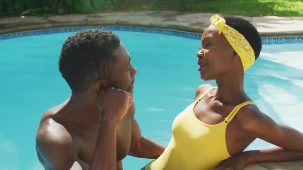 Happy african american couple standing in swimming pool talking and smiling in sunny garden