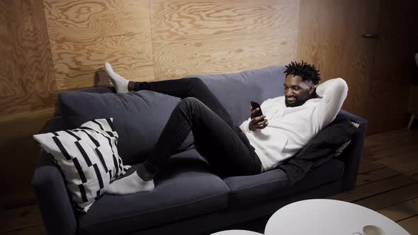 Black Man Resting on the Couch and Looking at the Phone