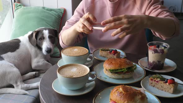 Woman Taking Photo Of Food Sitting In Cafe With Her Dog.