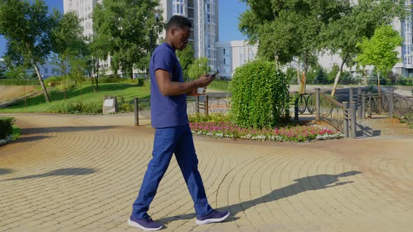 Afroamerican Man Uses Mobile Phone Holding White Cup with Coffee or Tea in Hand